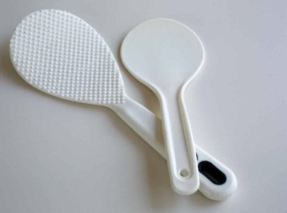 Close-up of a Rice Scoop with small dots next to a rice cooker filled with fluffy, perfectly cooked rice.